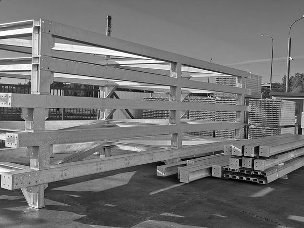 Stacked metal beams and frames at an outdoor storage yard under a clear blue sky.