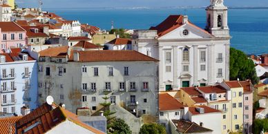 Scenic view of Lisbon's Alfama district with terracotta rooftops and a church by the blue Tagus River.