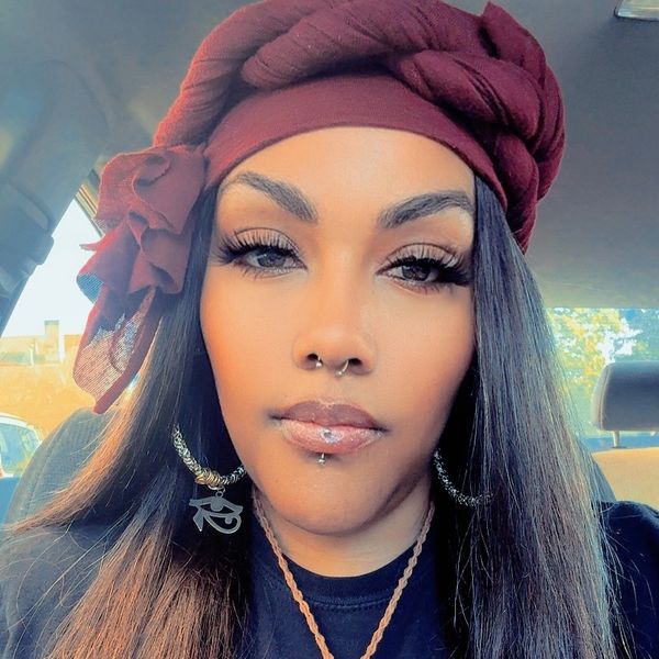 Woman with maroon headwrap and facial piercings in a car.