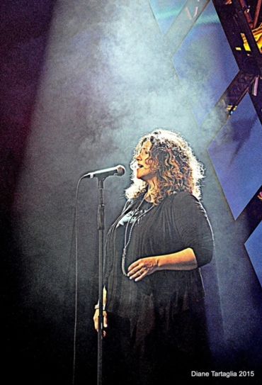 Woman singing passionately into a microphone on stage with dramatic lighting.