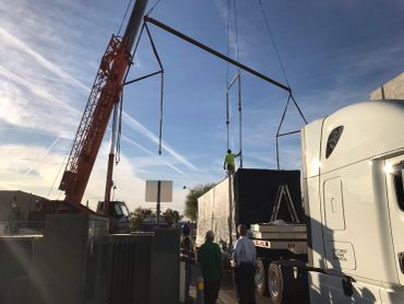 Crane lifting structure near truck with workers around.
