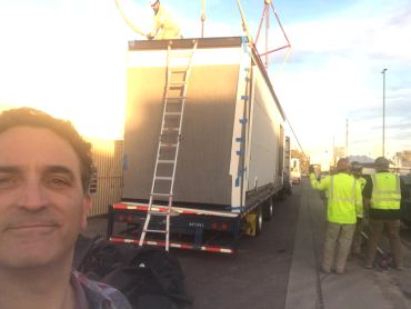 Man taking selfie near a trailer with construction workers.