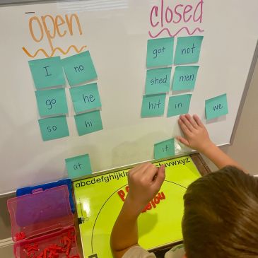 Child sorting word cards on a whiteboard labeled open and closed.