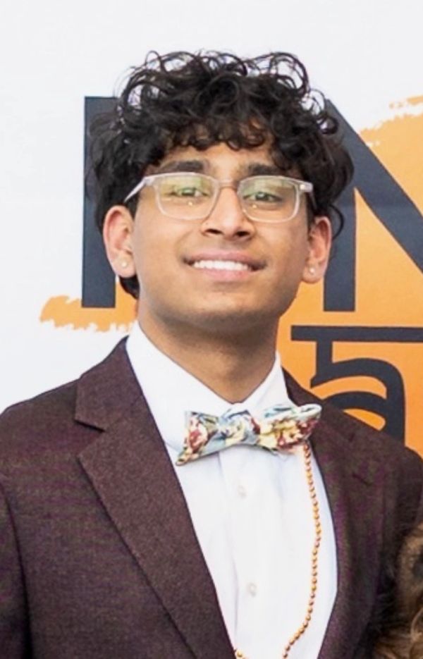Young man in a suit with glasses and a floral bow tie smiling.
