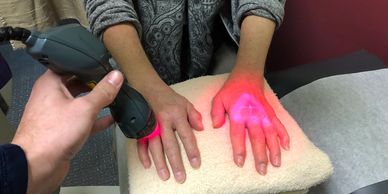 A patient sitting and receiving MLS Laser Therapy on her hands with both the robotic and handpiece.