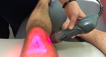A patient receiving MLS Laser therapy on their left knee from above the knee.