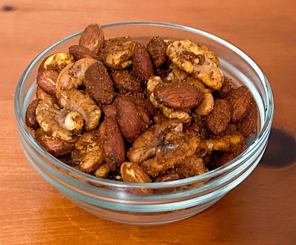 A glass bowl filled with mixed roasted nuts on a wooden surface.