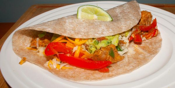 Chicken fajita wrap with cheese, guacamole, and lime on a white plate.
