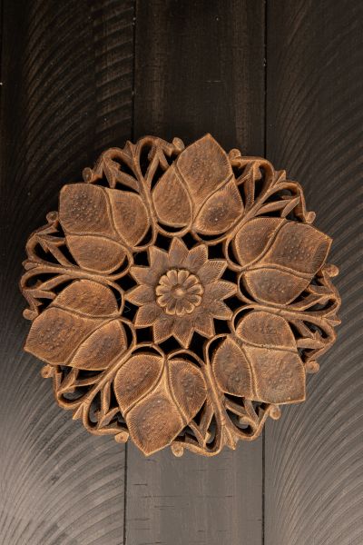 Intricately carved wooden floral design with leaf motifs on a dark surface.