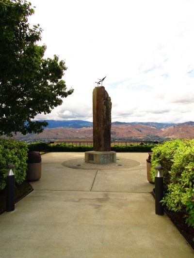 Stone monument with a bird sculpture on top overlooking mountains.