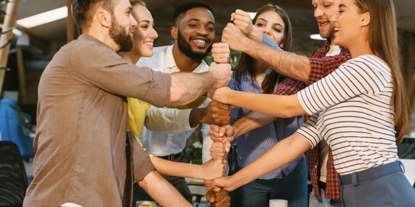 A group of colleagues joining hands in a team-building gesture and smiling.
