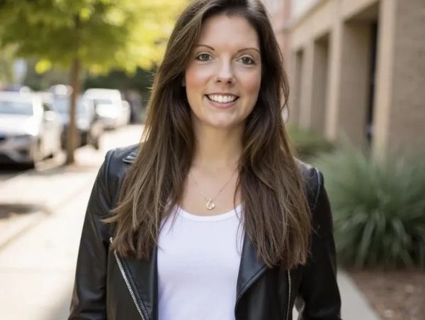 Smiling woman in a black leather jacket standing outdoors on a sunny day.