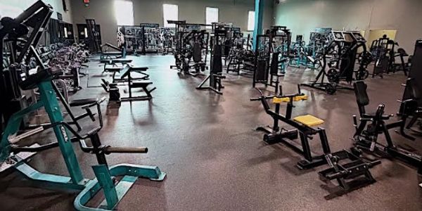 Empty gym filled with various workout machines and benches.