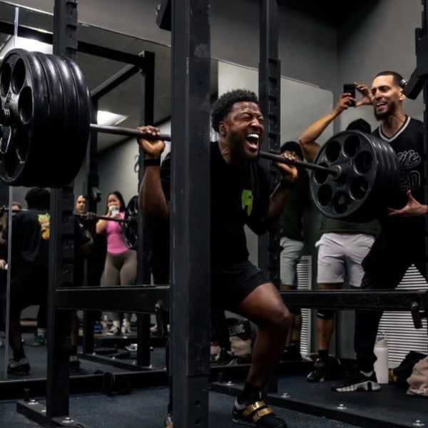 Man lifting heavy weights in gym with supporters around.