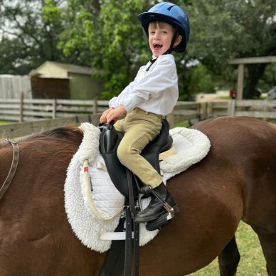 Young boy happily riding a brown horse wearing a helmet.