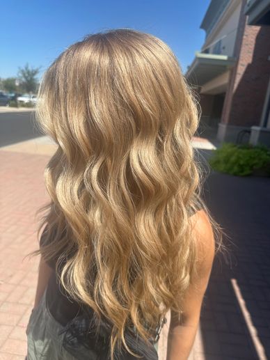 Sunlit wavy blonde hair flowing down a person's back outdoors.