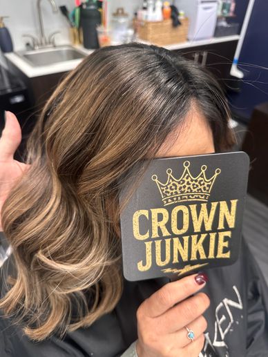 Woman with styled hair holding a 'Crown Junkie' sign covering her face.