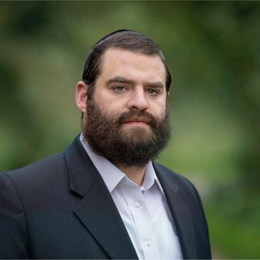 Bearded man in a suit with a thoughtful expression outdoors.