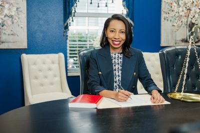 A confident woman in a blazer signing a document at a desk.