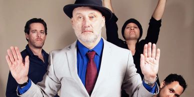 Four men posing, one in front wearing a hat and suit.