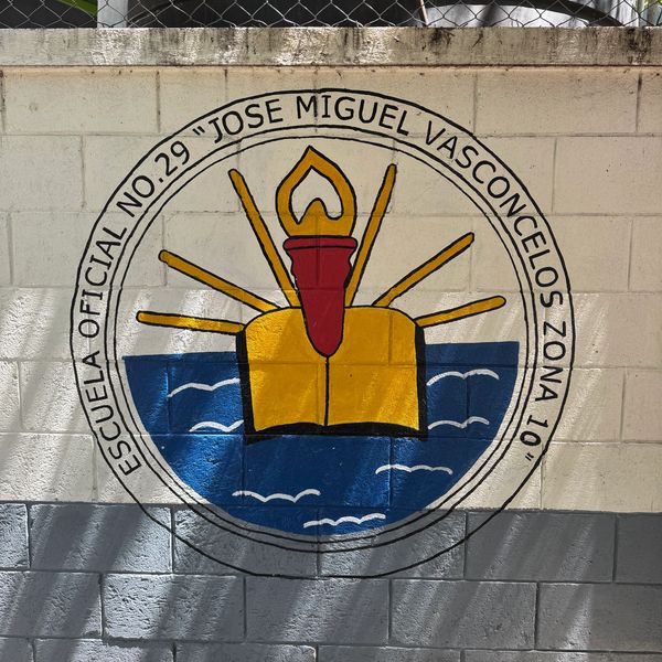 Mural of Escuela Oficial No. 29 Jose Miguel Vasconcelos with a torch and book symbol.
