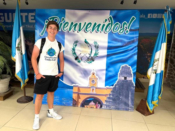 Young man standing in front of a Guatemalan welcome banner with flags.