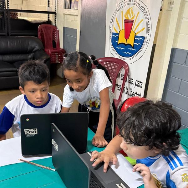 Three children working together on laptops at school.