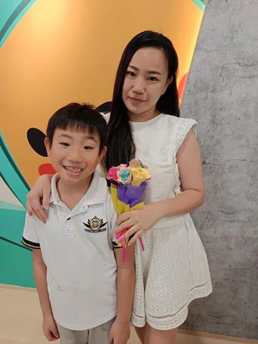 A woman in a white dress holding a colorful bouquet with a smiling boy beside her.