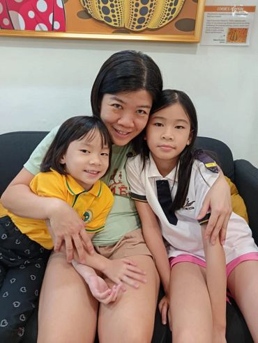 A mother with her two daughters sitting closely on a couch, smiling gently.