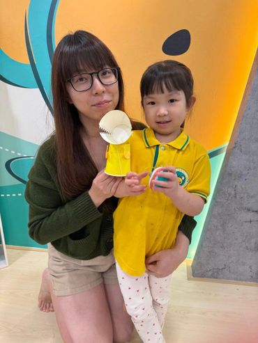Woman and child posing with a paper craft in a colorful room.