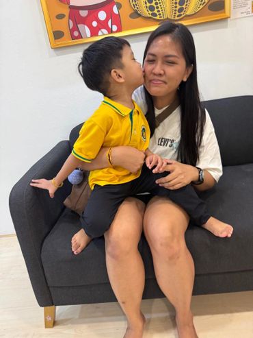 A young boy kisses a smiling woman sitting on a couch.