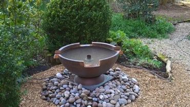 Garden pathway with a central water feature surrounded by stones and plants.