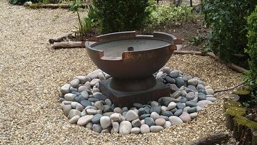 A bronze water feature surrounded by smooth stones in a garden.