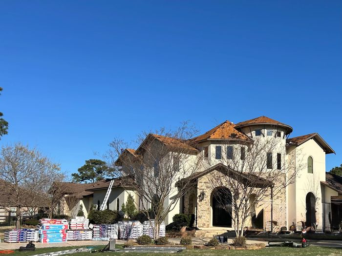 Large house undergoing roof renovation with materials stacked outside under clear sky.