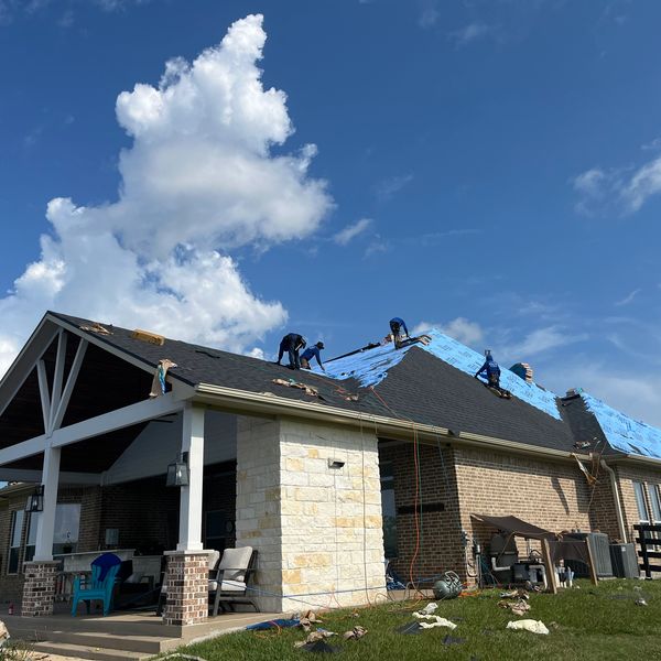 Workers installing a new roof on a suburban house under a partly cloudy sky.