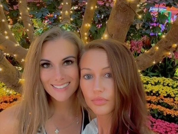 Two women posing with illuminated tree and flowers in the background.