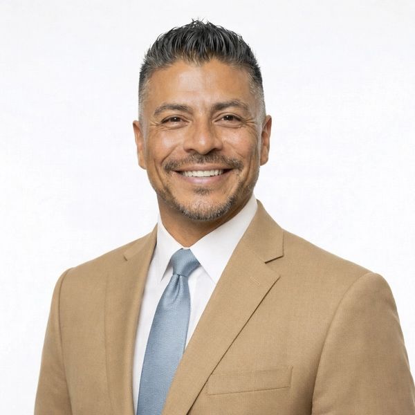 Smiling man in tan suit and blue tie against a white background.