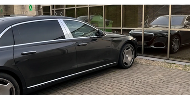 Zwarte luxe berline Mercedes Maybach S680 geparkeerd voor glazen gevel met spiegeling van de wagen