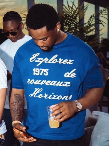 Man in a blue shirt looking at his phone and holding a drink.