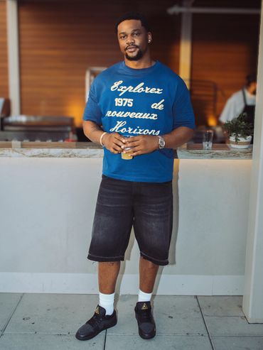 Man in casual blue shirt and black shorts holding a drink.