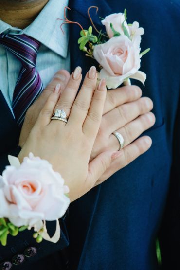 Close-up of wedding hands with rings and flowers.