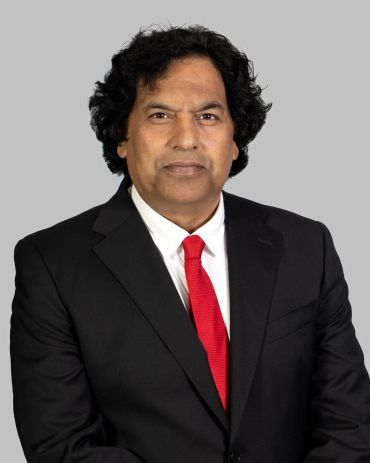 Man in black suit with red tie against gray background.