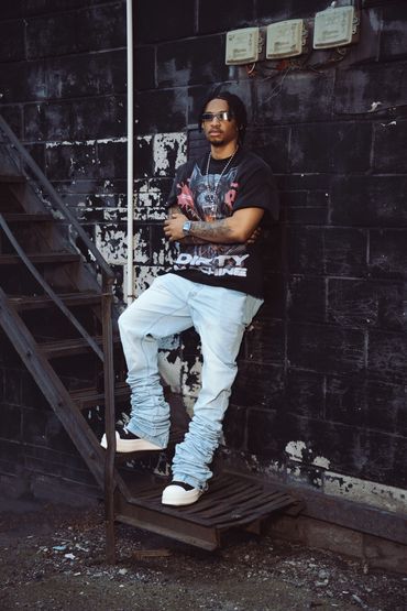 Man standing with crossed arms on a metal stair against a black wall.