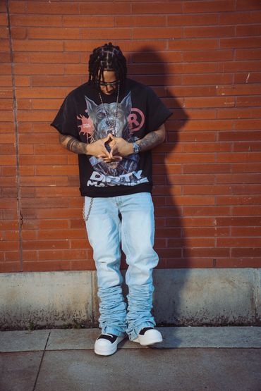 Man with braided hair looking down against brick wall.