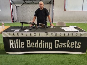 Man stands behind a Rifle Bedding Gaskets display table with a rifle.