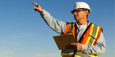 Construction worker in safety gear pointing and holding a clipboard.