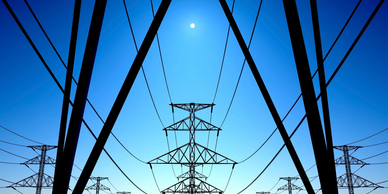 Electricity pylons silhouetted against a clear blue sky with the sun.