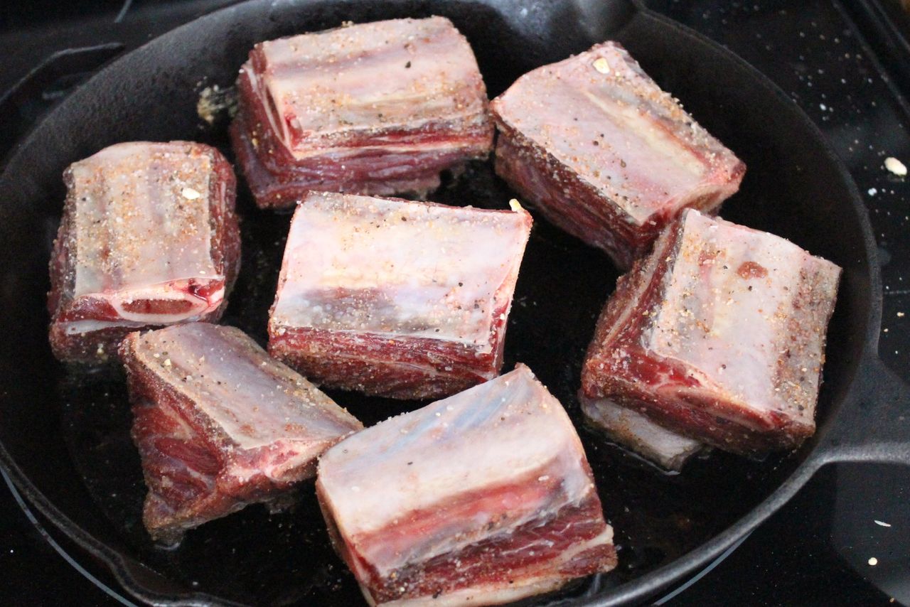 Seasoned bison short ribs cooking in a cast iron skillet
