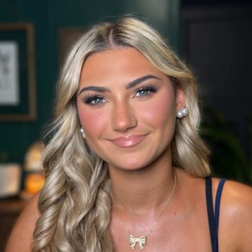 Smiling blonde woman with pearl earrings and a bow necklace.