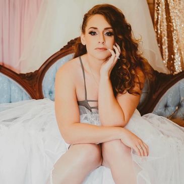 Woman in a white dress sitting on a vintage sofa with curly hair.